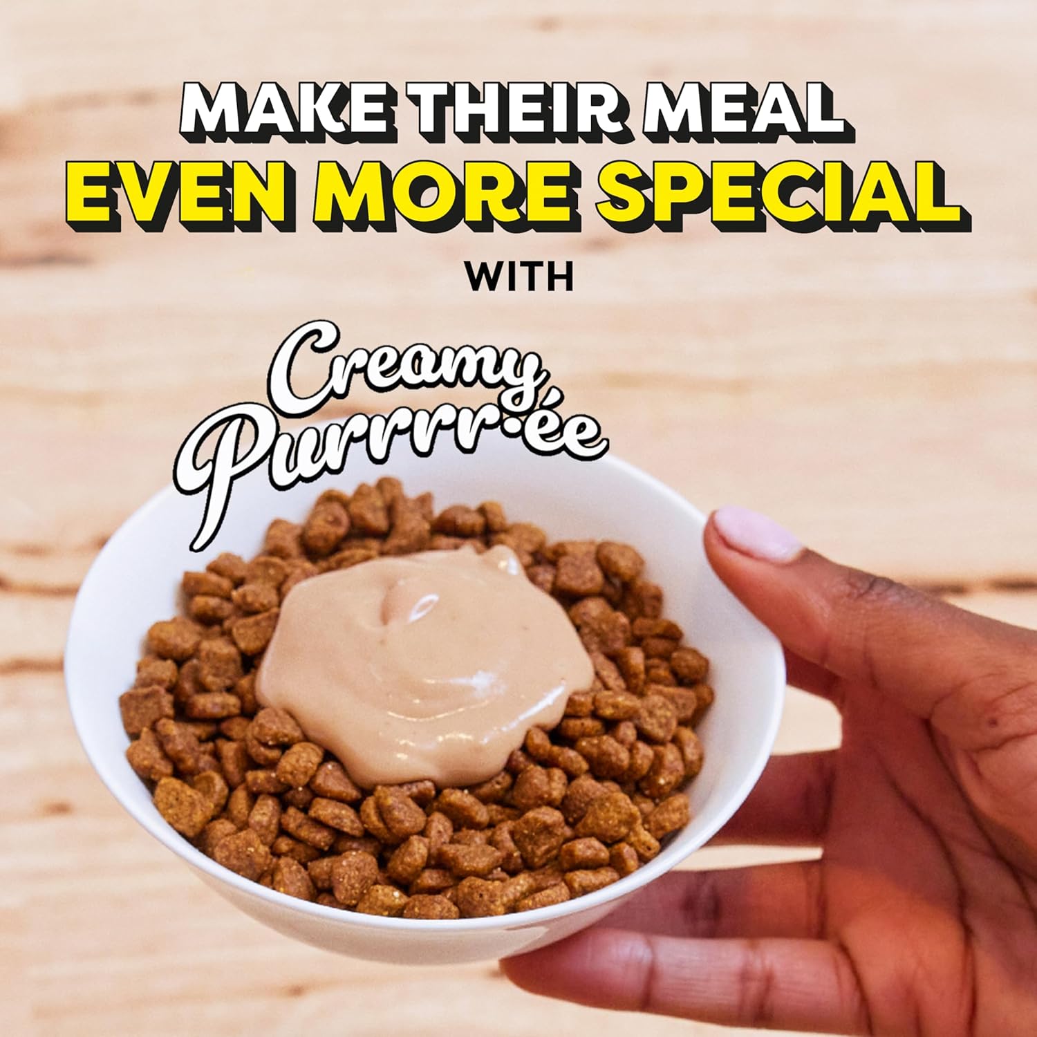 Hand holding a bowl of dog food with creamy purrree on a wooden surface